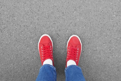 Photo of Woman in stylish gumshoes on asphalt, top view