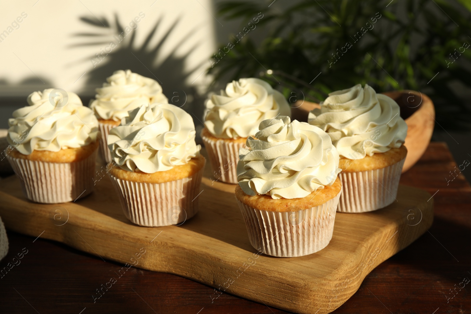 Photo of Tasty cupcakes with vanilla cream on wooden table, closeup