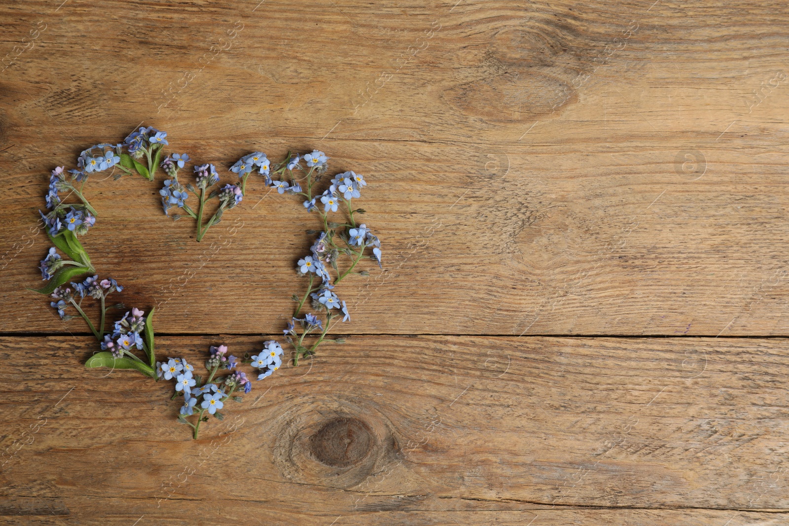 Photo of Heart made with beautiful forget-me-not flowers on wooden background, top view. Space for text