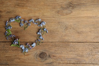 Heart made with beautiful forget-me-not flowers on wooden background, top view. Space for text