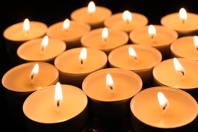 Photo of Wax candles burning on table in darkness, closeup