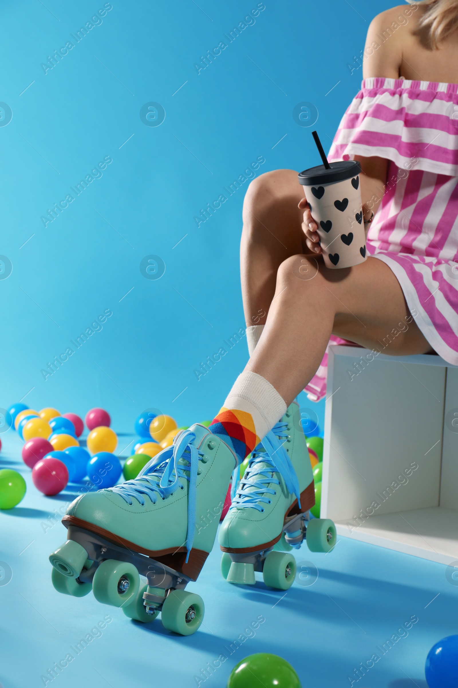 Photo of Young woman with retro roller skates and cup of drink on color background, closeup. Space for text