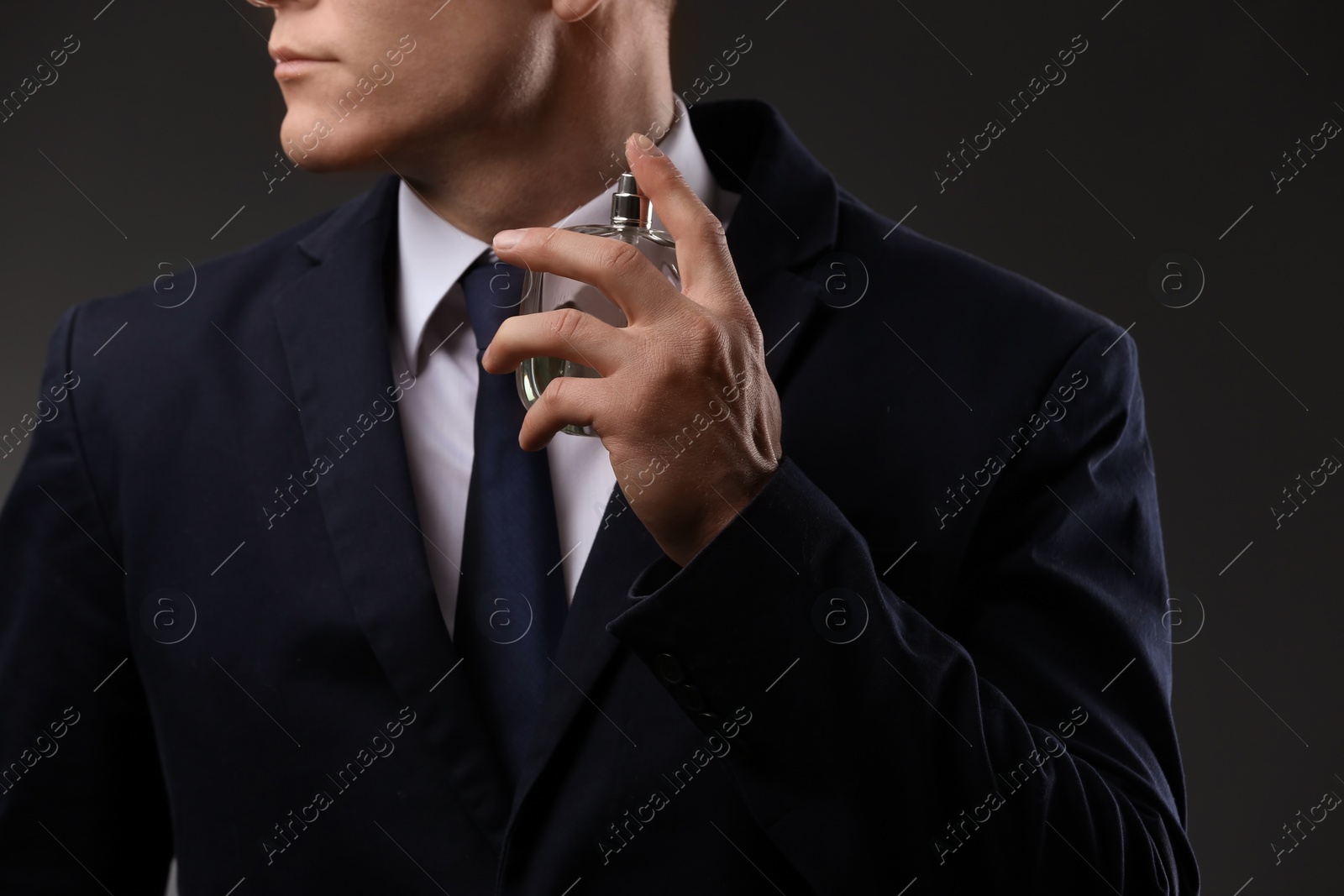 Photo of Handsome man in suit using perfume on dark background, closeup