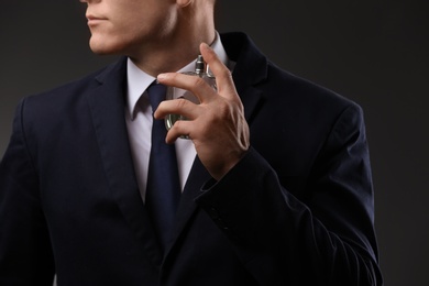 Handsome man in suit using perfume on dark background, closeup