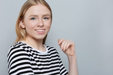 Portrait of beautiful young woman in striped t-shirt on grey background. Space for text