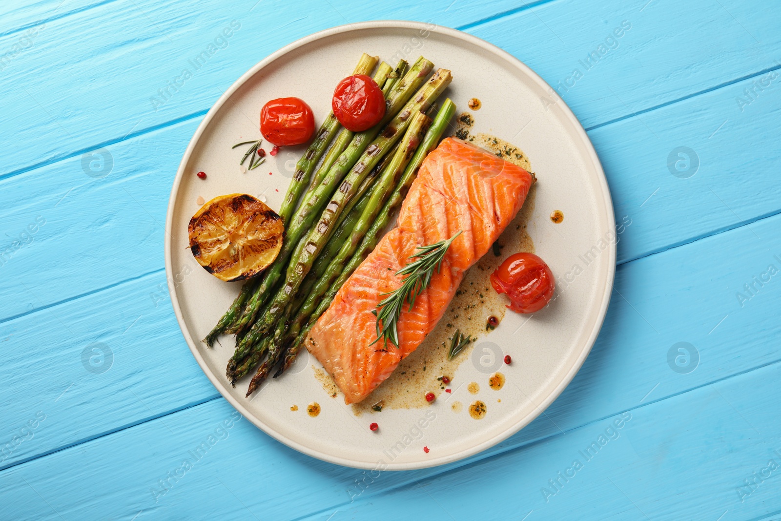 Photo of Tasty grilled salmon with asparagus, tomatoes and spices on light blue wooden table, top view