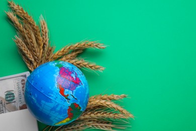 Import and export concept. Globe, ears of wheat and money on green background, flat lay. Space for text