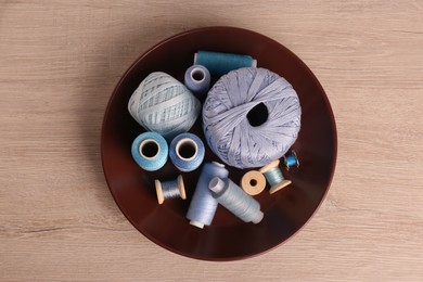 Color sewing threads in bowl on wooden table, top view