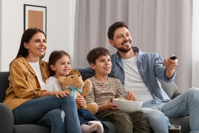 Happy family watching TV at home. Father changing channels with remote control