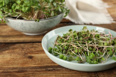 Photo of Plate with fresh radish microgreens on wooden table, space for text