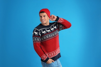 Photo of Handsome man in Christmas sweater and hat on blue background