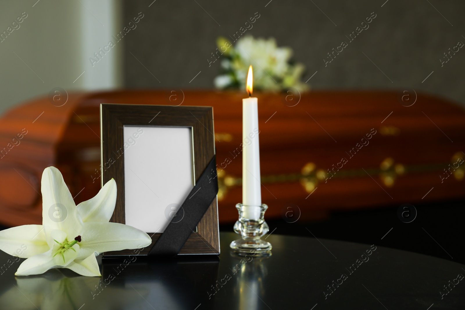 Photo of Black photo frame with burning candle and white lily on table in funeral home