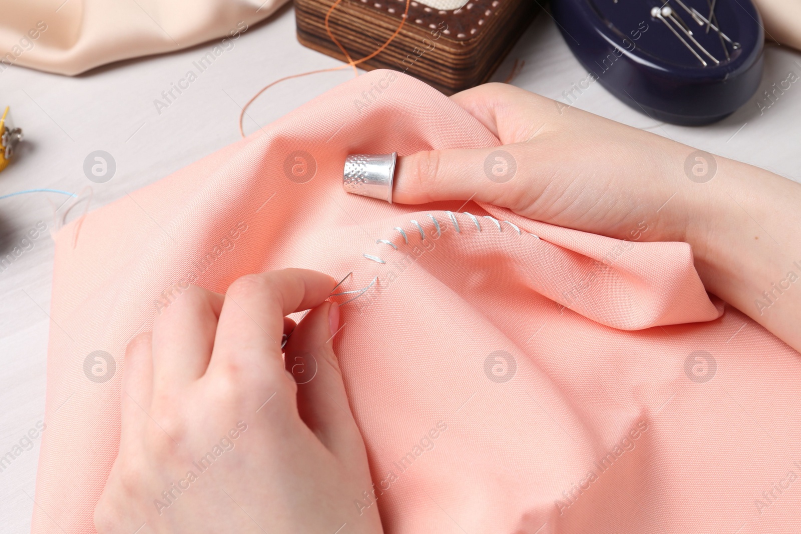 Photo of Woman with sewing needle and thread embroidering on cloth at white wooden table, closeup