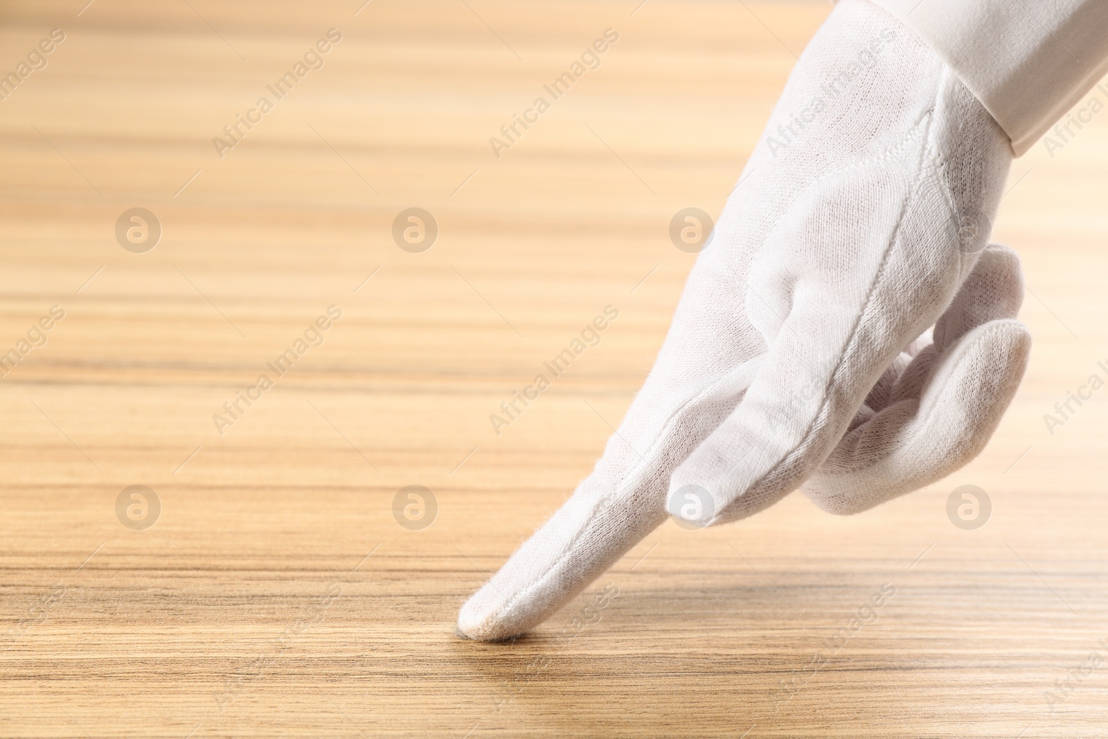 Photo of Person in white glove checking cleanliness of wooden  table, closeup. Space for text