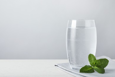 Photo of Glass of soda water, mint and napkin on white wooden table. Space for text