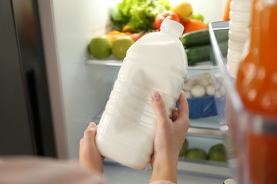 Photo of Woman with gallon of milk near refrigerator indoors, closeup