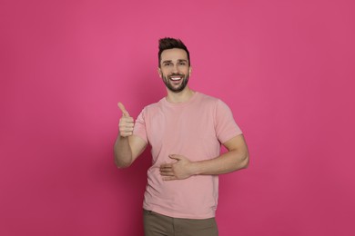 Photo of Happy man touching his belly and showing thumb up on pink background. Concept of healthy stomach