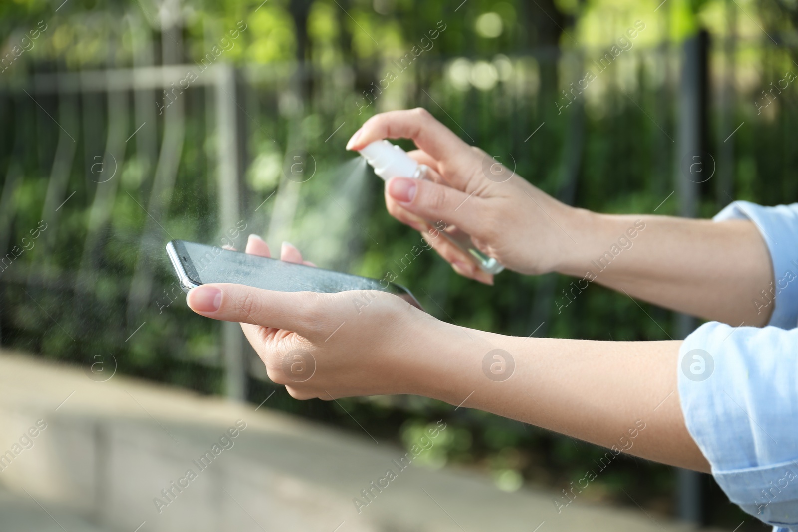 Photo of Woman spraying antiseptic onto smartphone outdoors, closeup