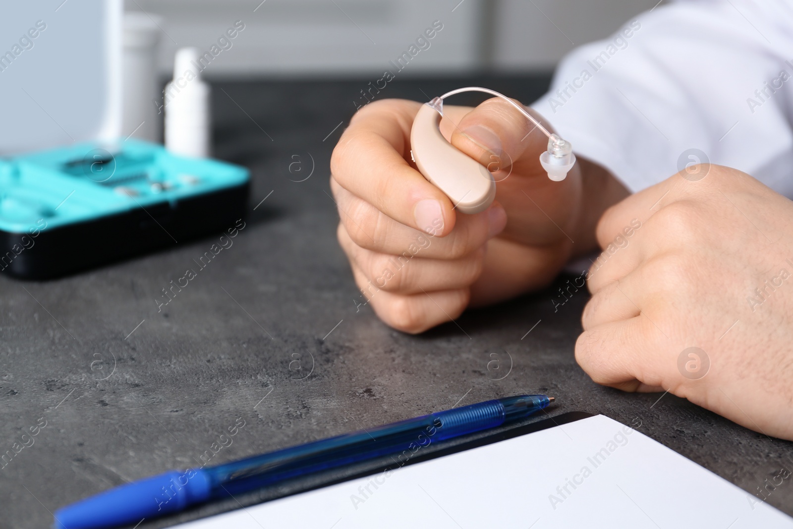 Photo of Doctor holding hearing aid at table, closeup with space for text. Medical objects