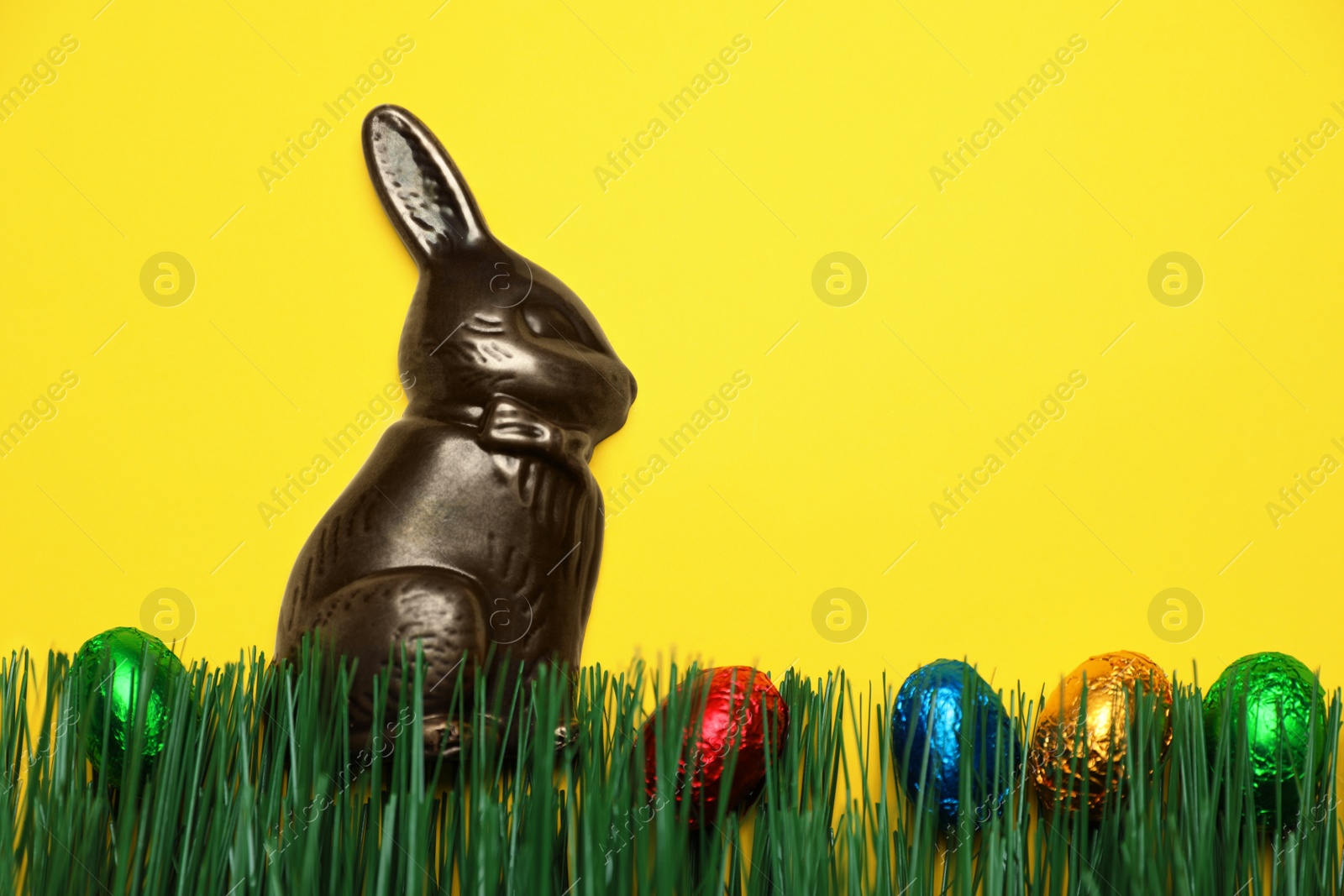 Photo of Chocolate Easter bunny and eggs with green grass on yellow background. Space for text