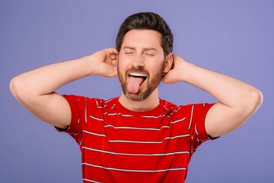 Emotional man showing his tongue on violet background