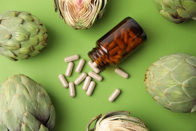 Photo of Bottle with pills and fresh artichokes on light green background, flat lay
