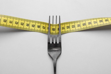 Photo of Fork with measuring tape on white background, top view. Diet concept