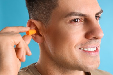 Photo of Man inserting foam ear plug on light blue background, closeup