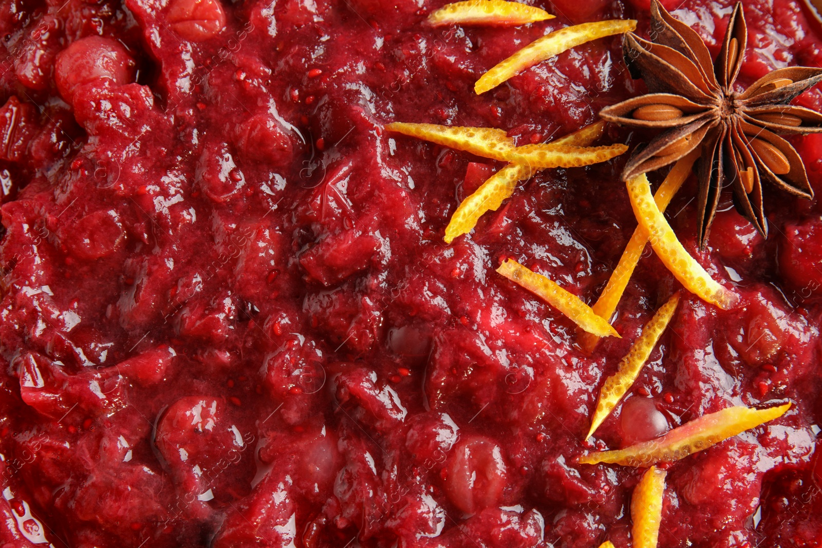 Photo of Tasty cranberry sauce with citrus zest and anise as background, top view