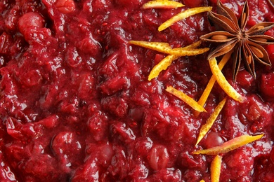 Tasty cranberry sauce with citrus zest and anise as background, top view