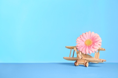 Photo of Wooden plane and flower on table against color background, space for text. International Women's Day