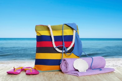 Image of Stylish striped bag and other beach accessories on wooden table near sea