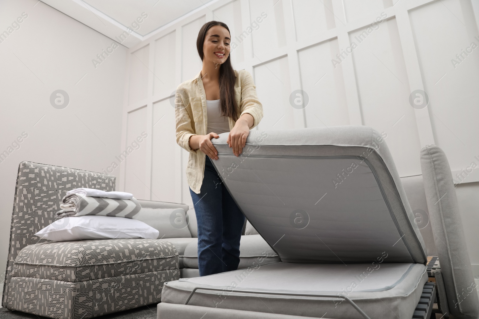 Photo of Woman making sleeping place for guest in living room. Convertible sofa