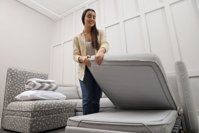 Woman making sleeping place for guest in living room. Convertible sofa