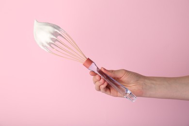 Photo of Woman holding whisk with whipped cream on pink background, closeup