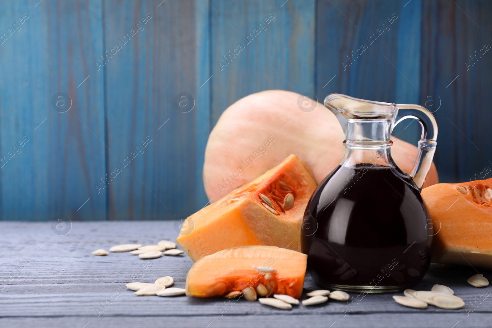 Photo of Fresh pumpkin seed oil in glass jug on grey wooden table. Space for text