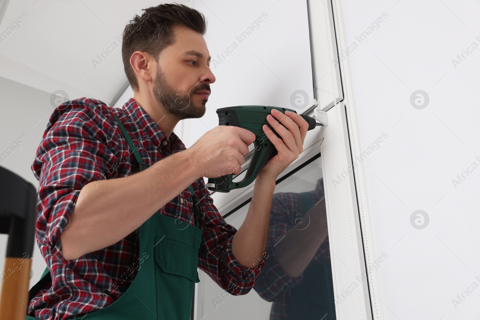 Photo of Worker in uniform installing roller window blind indoors