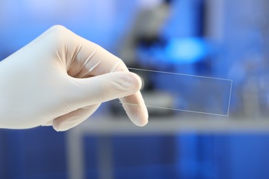 Scientist holding clean glass microscope slide in laboratory, closeup