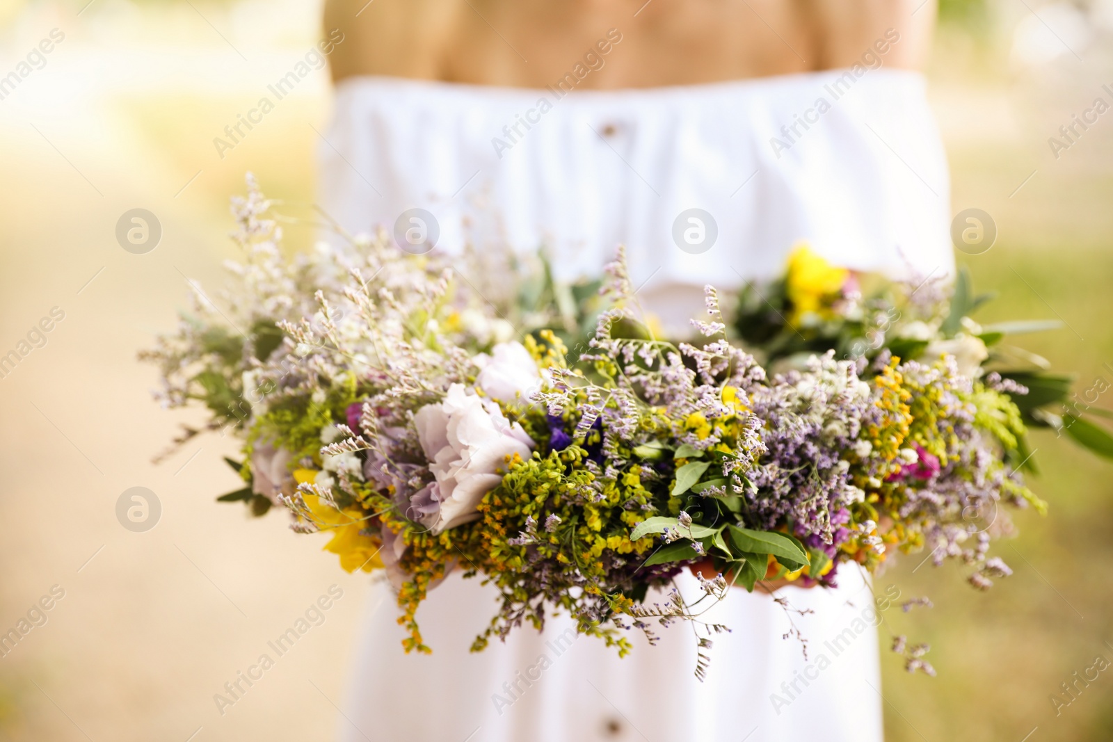 Photo of Young woman holding wreath made of beautiful flowers outdoors on sunny day, closeup