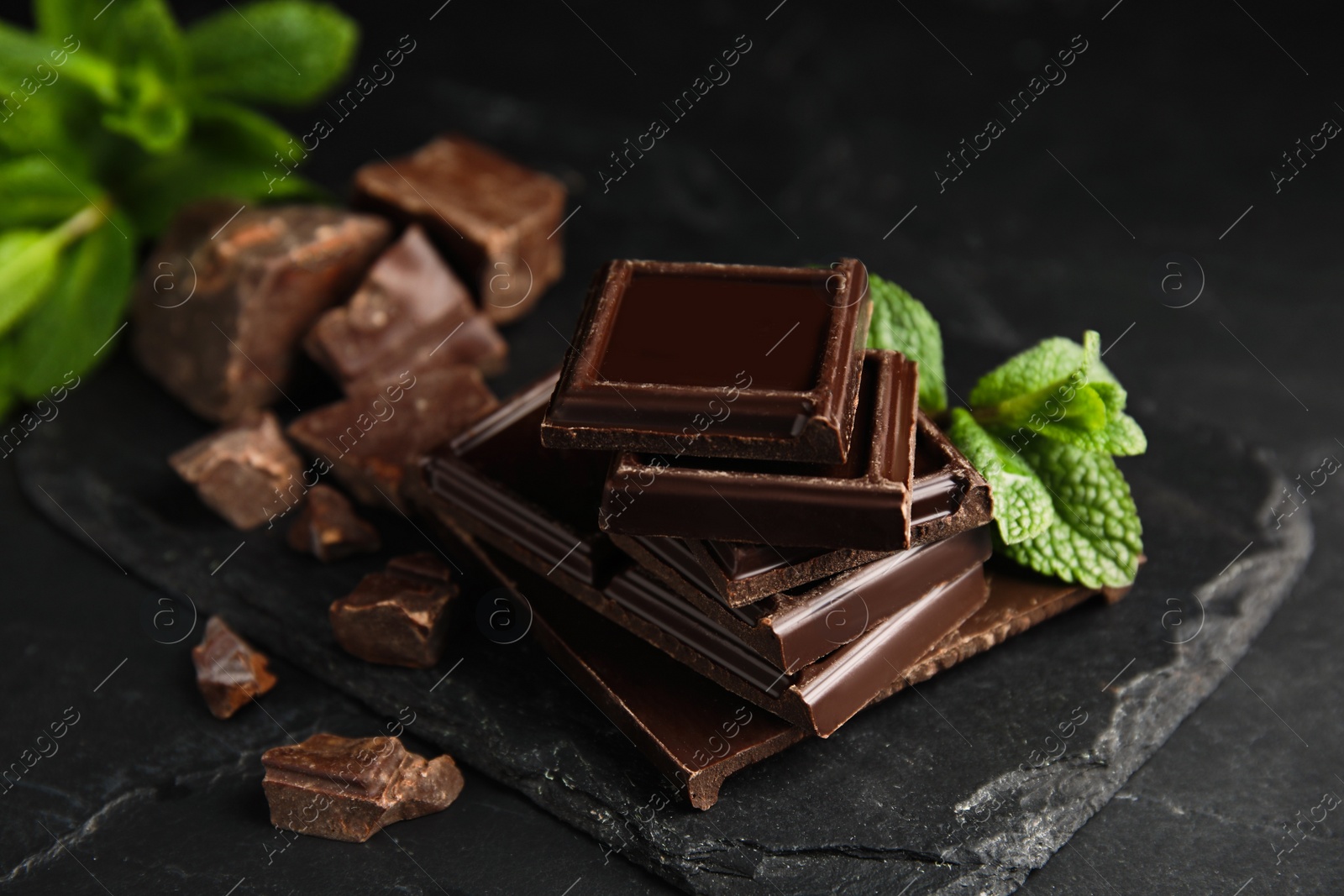 Photo of Tasty chocolate pieces and mint on black table, closeup