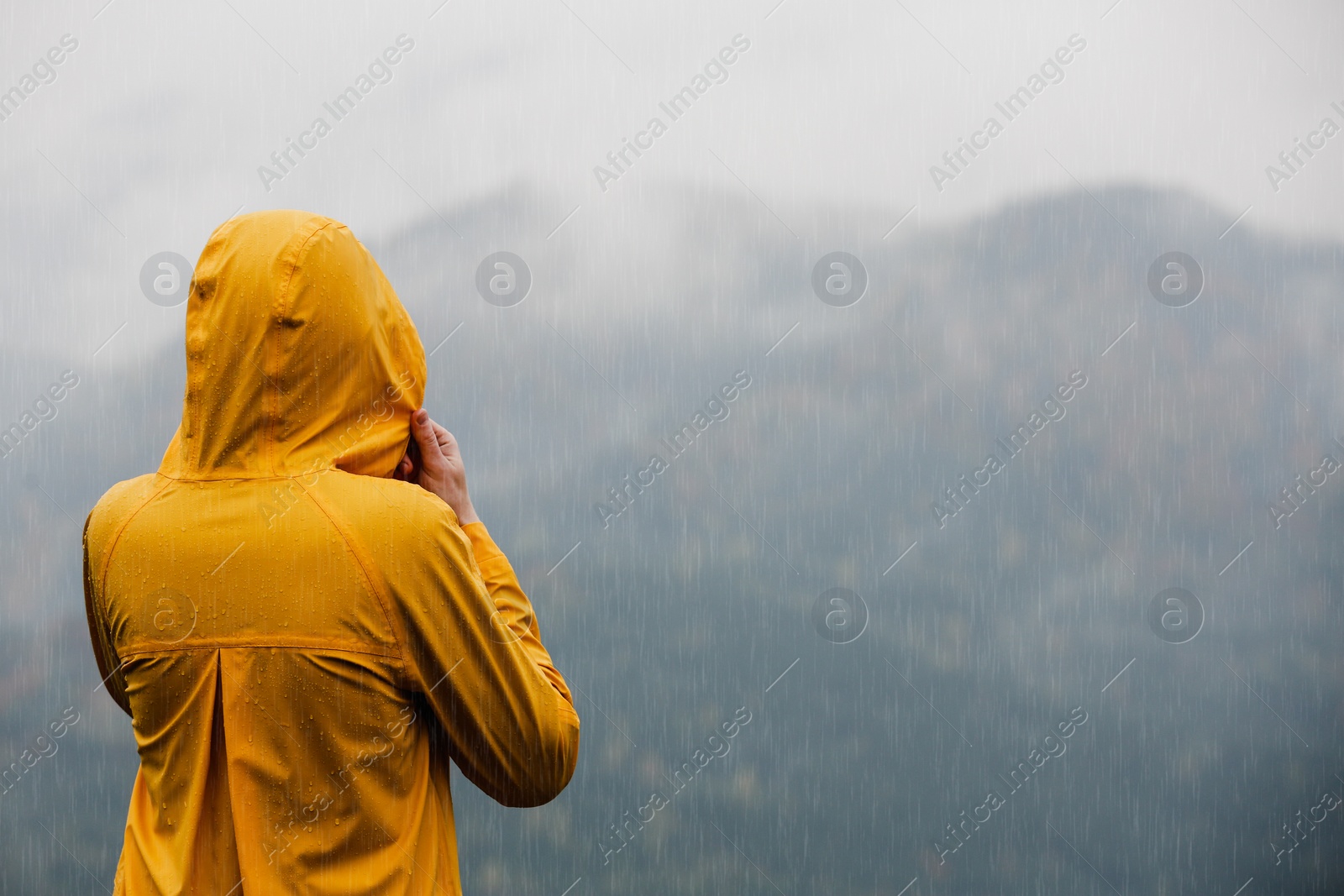 Photo of Woman in raincoat enjoying mountain landscape under rain, back view