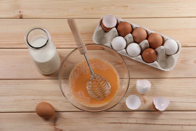 Photo of Making dough. Beaten eggs in bowl, shells and milk on wooden table, flat lay