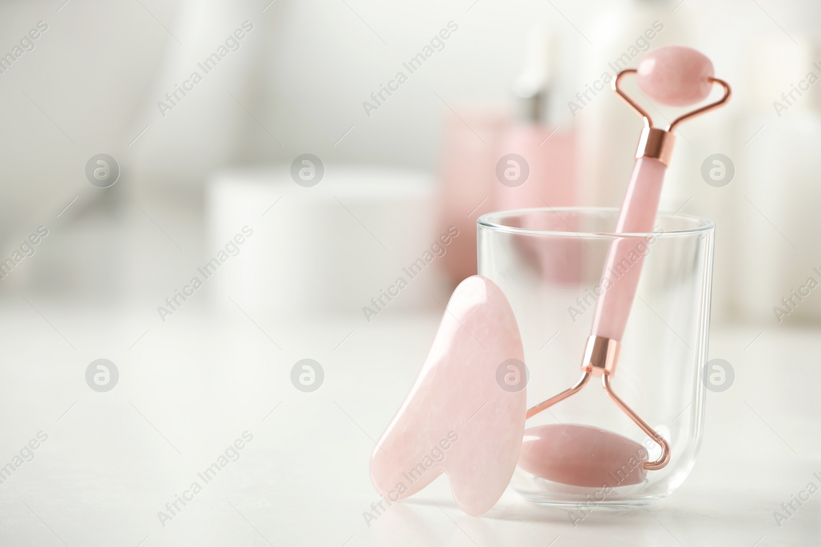 Photo of Natural face roller and gua sha tool on white table against blurred background, closeup. Space for text