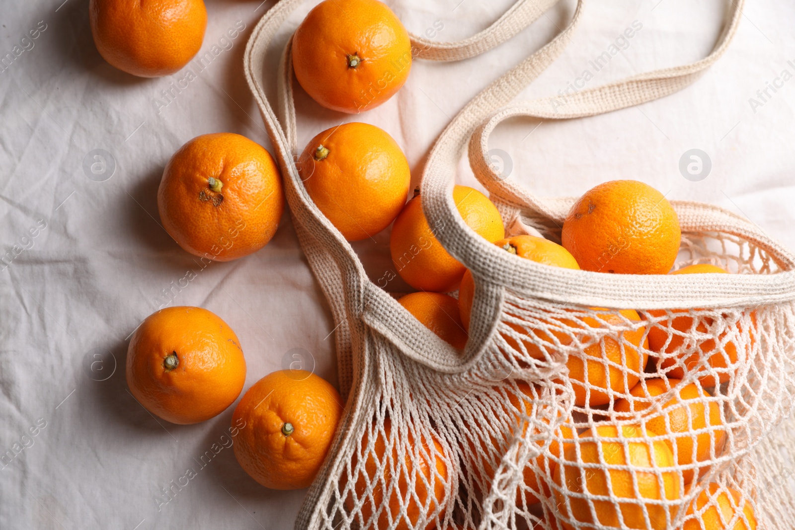 Photo of Net bag with many fresh ripe tangerines on white cloth, flat lay