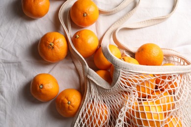 Photo of Net bag with many fresh ripe tangerines on white cloth, flat lay