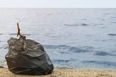 Photo of Trash bag full of garbage on beach. Space for text