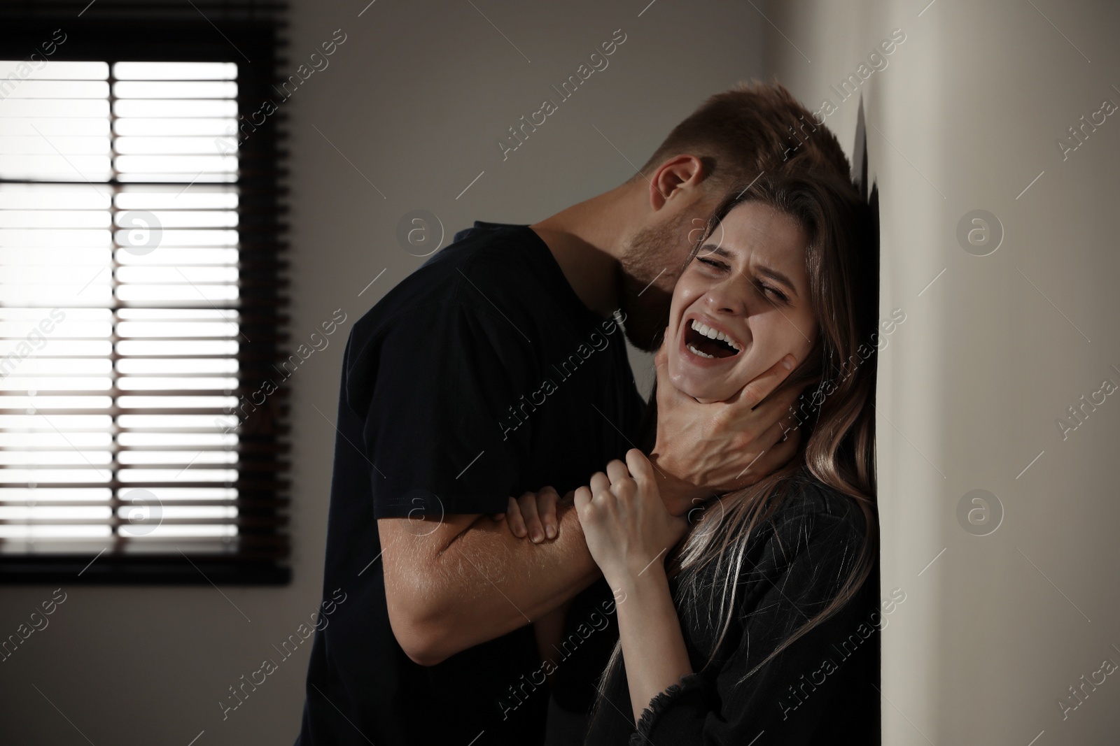 Photo of Man choking young woman indoors. Stop sexual assault