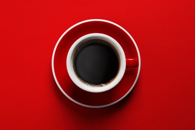 Cup with aromatic coffee on red background, top view