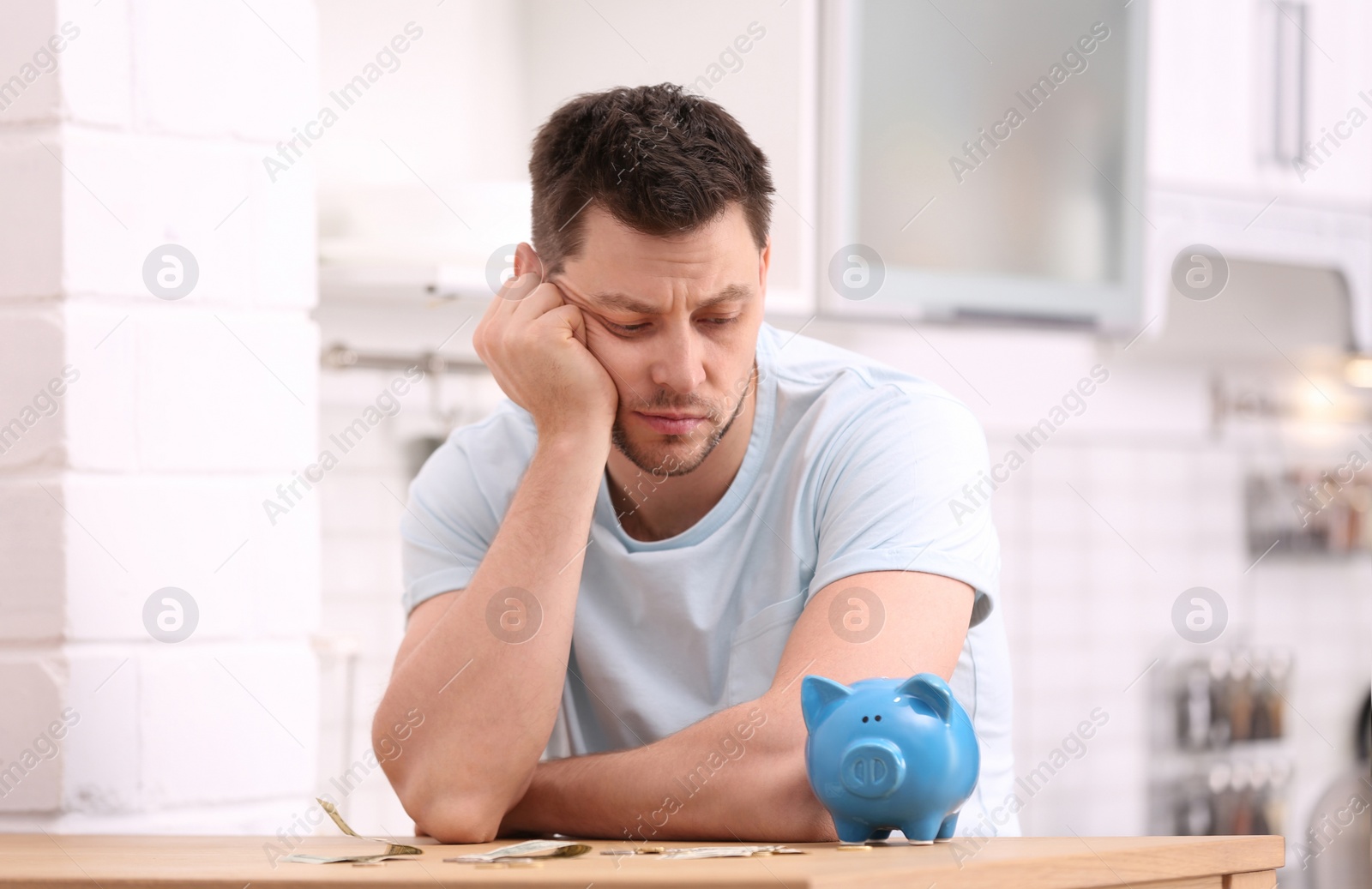 Photo of Sad man with piggy bank and money at home