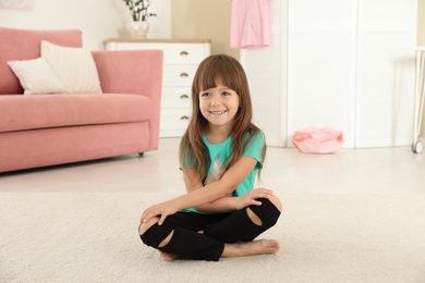 Photo of Cute little girl sitting on carpet at home